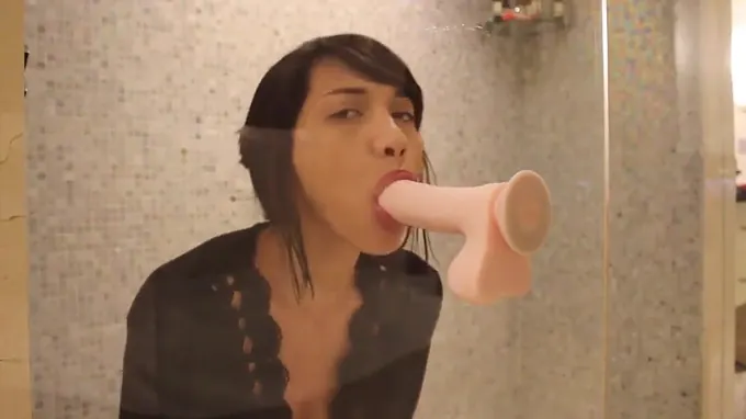 Naked brunette is in the shower and is sucking a huge dildo