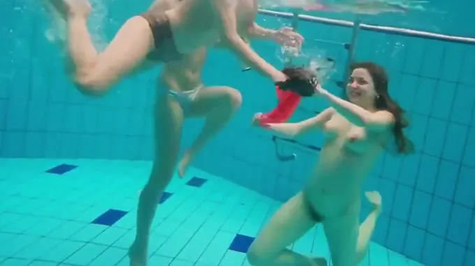 Three playful babes swimming in the pool and taking off their bikini
